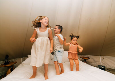 Children playing joyfully on a bed in a tent.