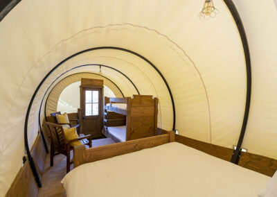 Cozy glamping tent interior with beds and wooden furniture.