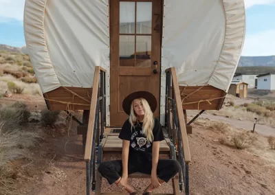 Woman sitting on covered wagon steps outdoors.