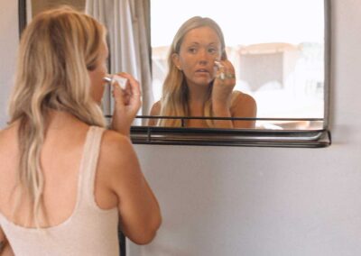 Woman applying makeup in bathroom mirror.