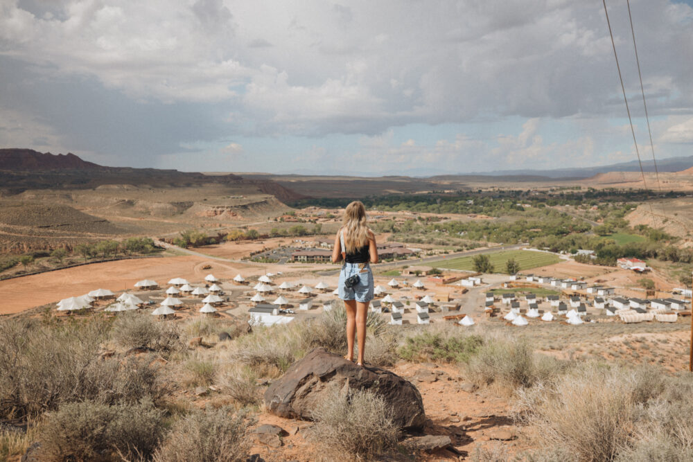 Woman overlooking desert landscape with tents and hills.